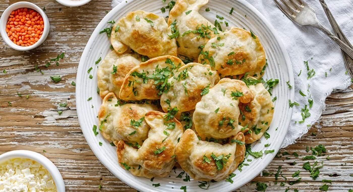 Pierogi na talerzu ze szczypiorkiem, białym serem i soczewicą - zdjęcie.