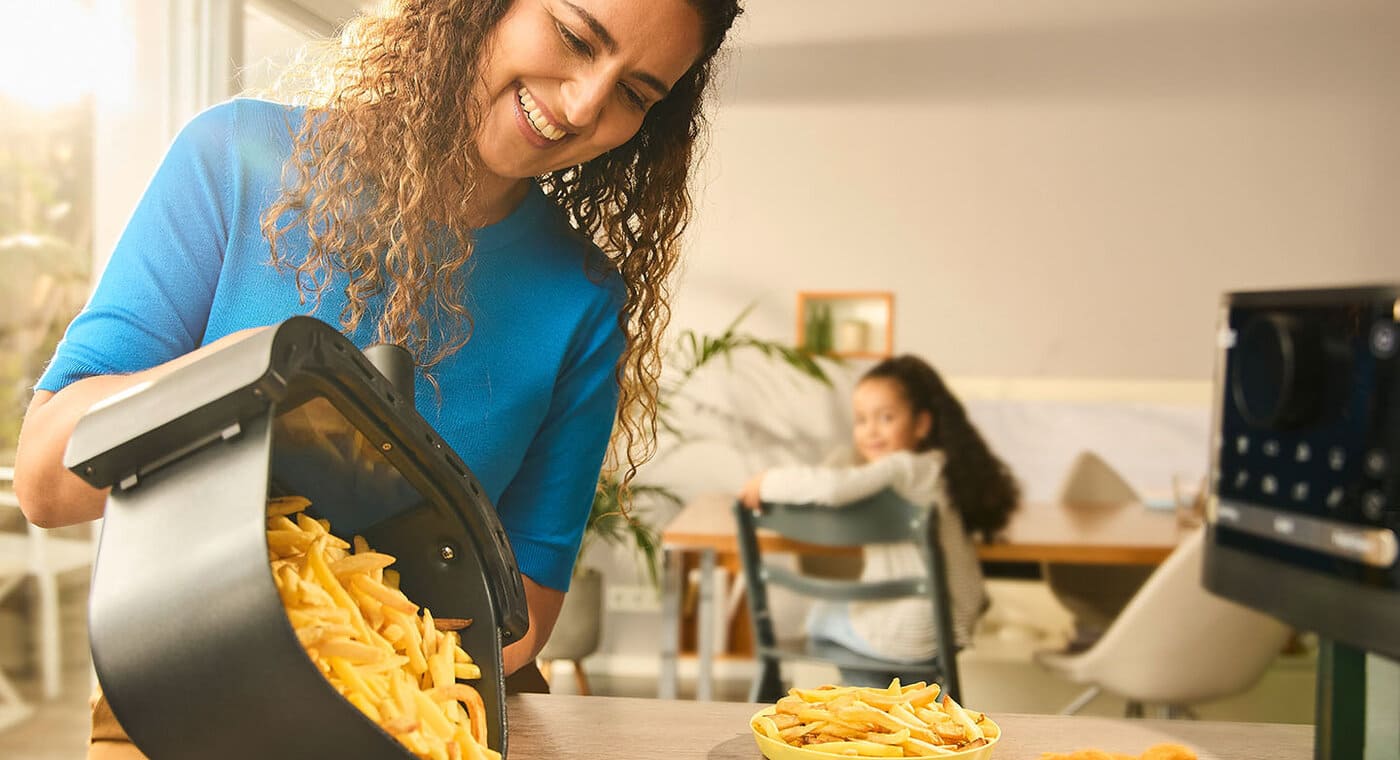 Kobieta wysypująca frytki przygotowane we frytkownicy na talerz