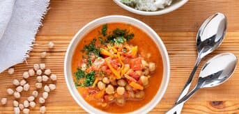 Top view of a wooden table with a soup plate with chickpea coconut curry and a bowl of rice.