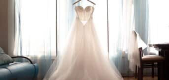 Tiulowa suknia ślubna wisząca na wieszaku na tle okna