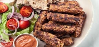 Kebabczety na talerzu z warzywami i sosem - zdjęcie.