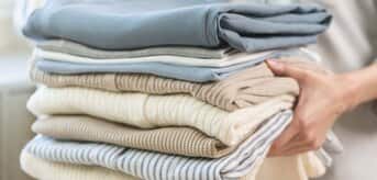 Osoba trzymająca stos starannie poskładanych ubrań w neutralnych kolorach. - zdjęcie