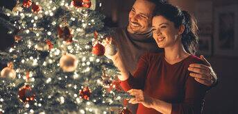 A brunette woman and man decorating a christmas tree together, with big smiles on their faces
