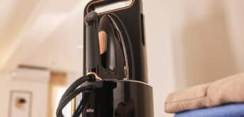 Generator pary Braun CareStyle 9 w stacji bazowej, ustawione na stole obok poskładanych ubrań. - zdjęcie