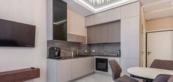 Nowoczesna kuchnia z aneksem, z eleganckimi szarymi meblami i designerskimi krzesłami przy okrągłym stole. - tytułowa