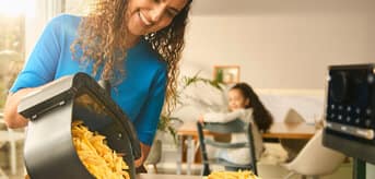 Kobieta wysypująca frytki przygotowane we frytkownicy na talerz