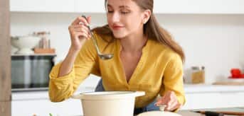 Kobieta wąchająca rosół w garnku - zdjęcie.