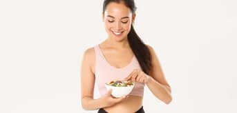 Kobieta w sportowym stroju jedząca sałatkę.