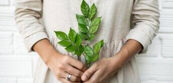 Kobieta ubrana w lnianą sukienkę trzymająca zielone gałązki