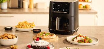 Braun MultiFry 5 Air fryer standing on a kitchen counter, alongside a cake, fries, grilled meat and a pizza