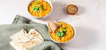 Two bowls of yellow curry on a white surface.