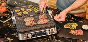 A man grilling steak alongside colorful vegetables