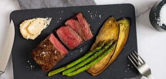 Na talerzu pokrojona wołowina, ze szparagami, bakłażanem, solą, pieprzem i masłem. - zdjęcie