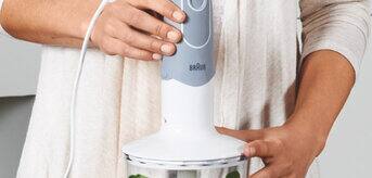 A woman blending food in a kitchen with a Braun Hand blender.