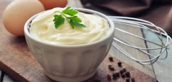 Domowy majonez w miseczce stojącej na desce do krojenia