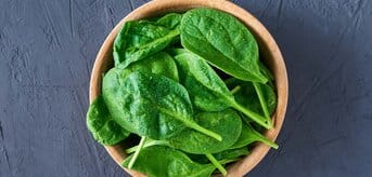 Liście szpinaku leżące w drewnianej miseczce na szarym podłożu