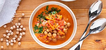 Top view of a wooden table with a soup plate with chickpea coconut curry and a bowl of rice.