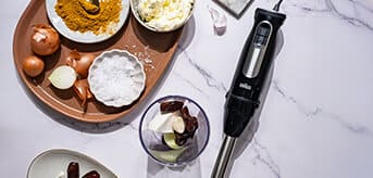 Top view of a white marble plate with the MultiQuick 9 hand blender and ingredients for an oriental dip made from dates, garlic, cream cheese, onions and curry