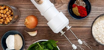 View from above of a wooden table on which the white MultiQuick 7 with double whisk attached lies next to small bowls with ingredients and spices