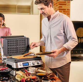 A man and woman are preparing a meal together in a modern kitchen, surrounded by various cooking utensils and ingredients