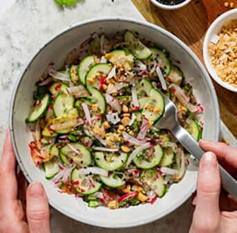 View from above of a white marble table with a bowl filled with fresh Thai cucumber salad.