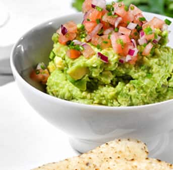 A white bowl of guacamole with a topping of diced tomatoes and onions
