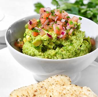 Biela miska guacamole s nakrájanými paradajkami a cibuľou