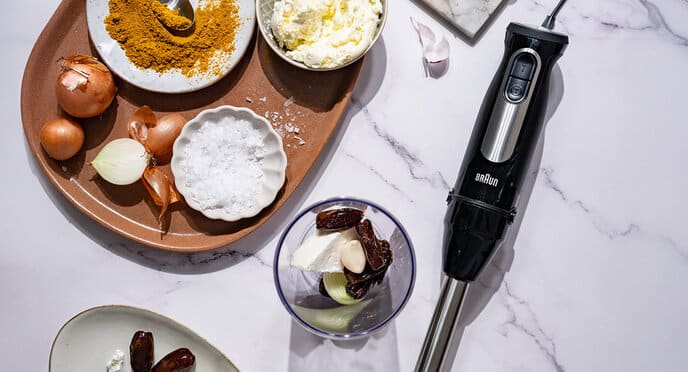Top view of a white marble plate with the MultiQuick 9 hand blender and ingredients for an oriental dip made from dates, garlic, cream cheese, onions and curry