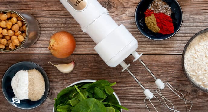 View from above of a wooden table on which the white MultiQuick 7 with double whisk attached lies next to small bowls with ingredients and spices