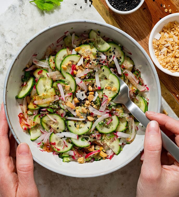 View from above of a white marble table with a bowl filled with fresh Thai cucumber salad.